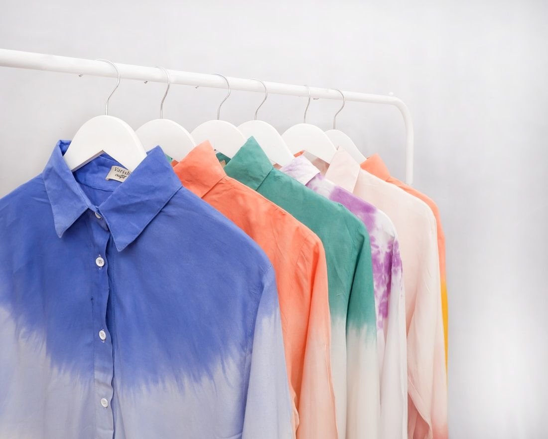 Dip-dyed shirts graded from pale to deep colour hanging on a white rail