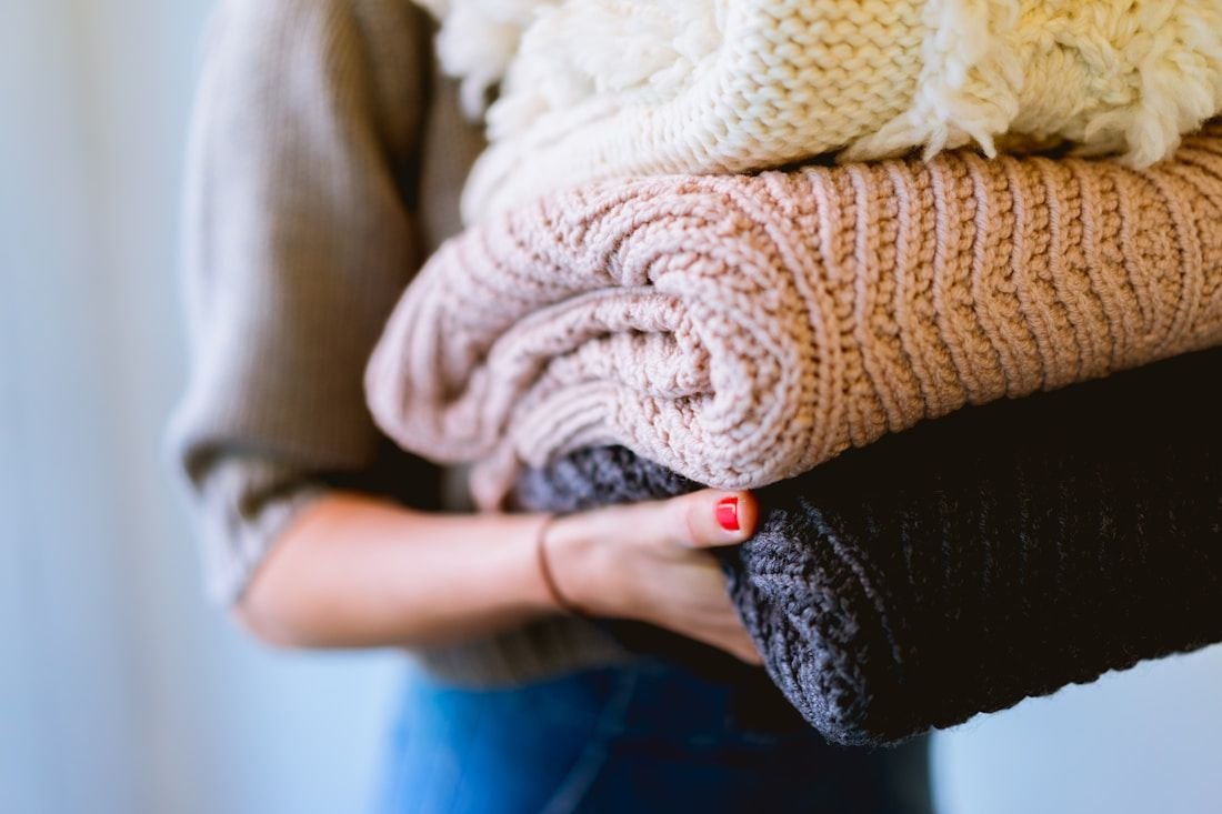 Person carrying a neatly folded stack of soft cream and blush garments
