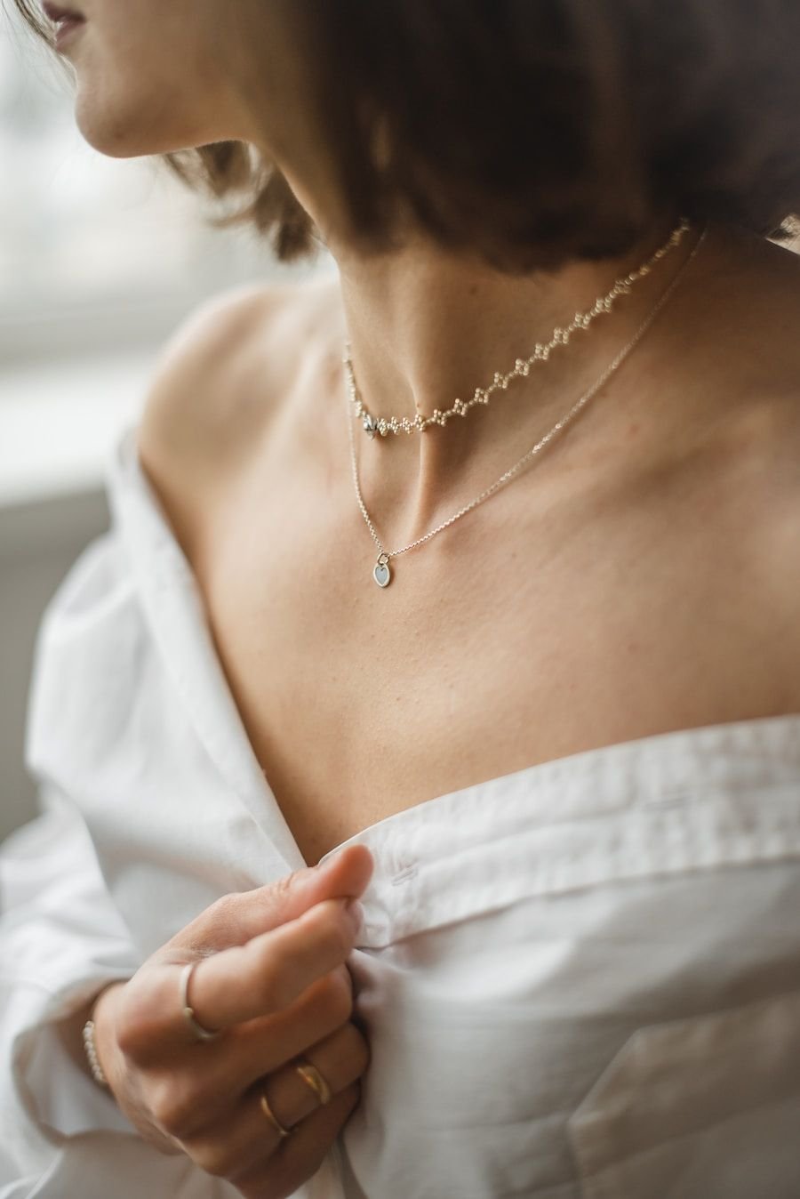 Close detail of a bare shoulder, a fine chain necklace and a white off-shoulder top