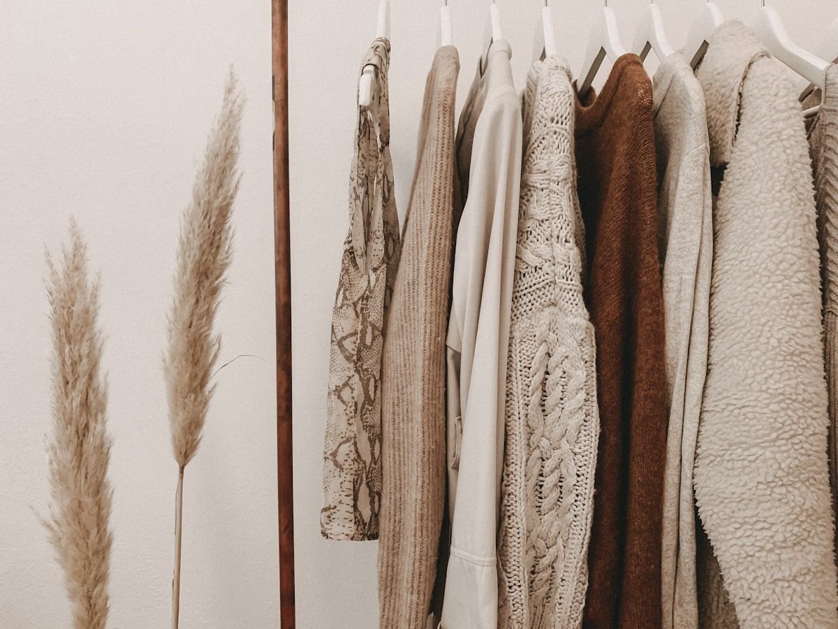 Neutral coats and knitwear hanging beside tall dried pampas grass