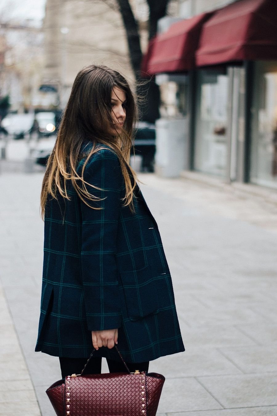 Woman in a long dark coat walking a quiet street carrying a structured bag