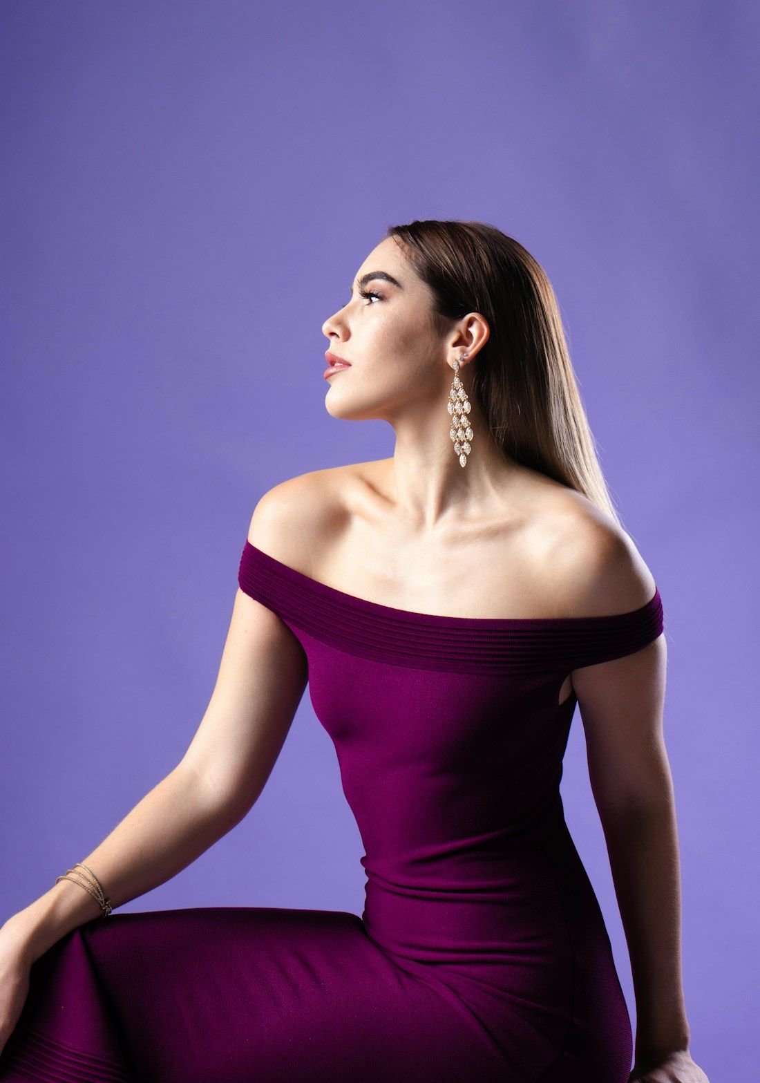 Woman in a deep plum off-shoulder satin gown, photographed against a plain studio backdrop